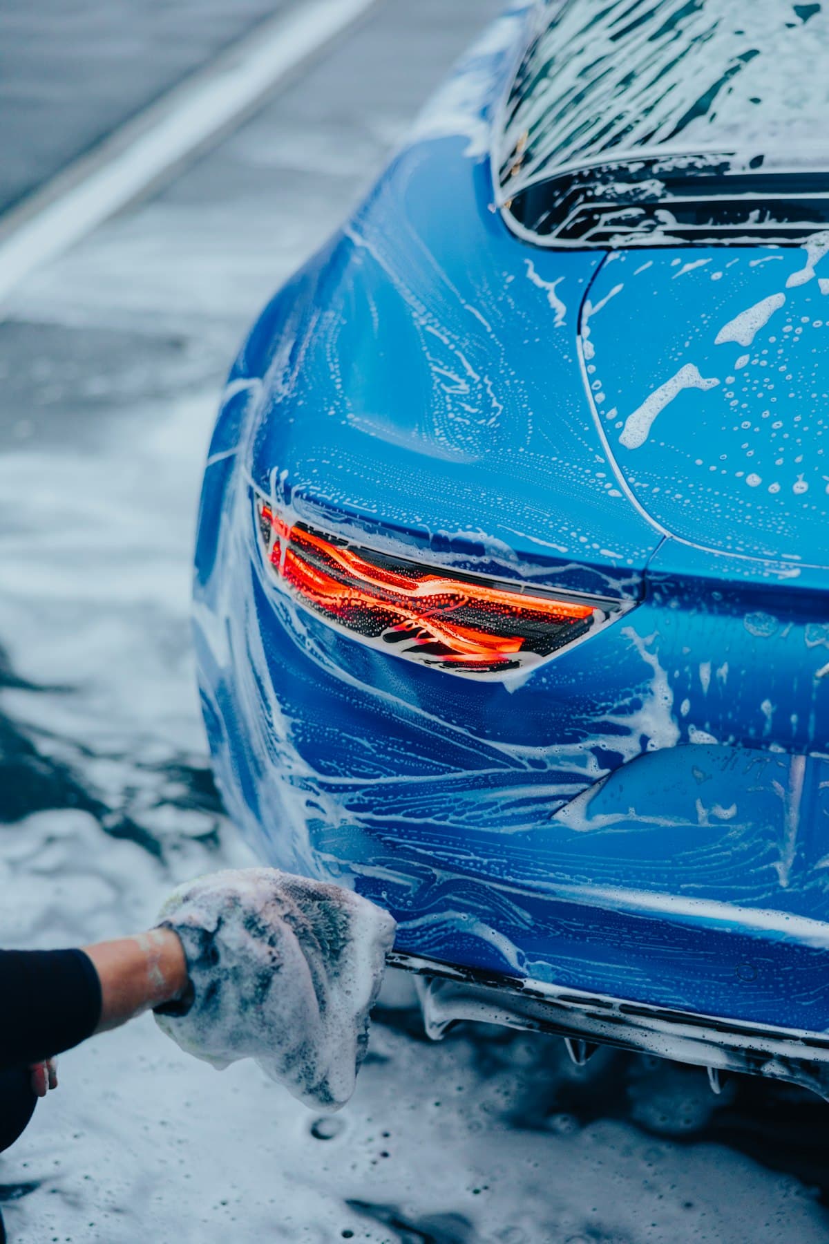 Hand washing a blue car with microfiber mitt